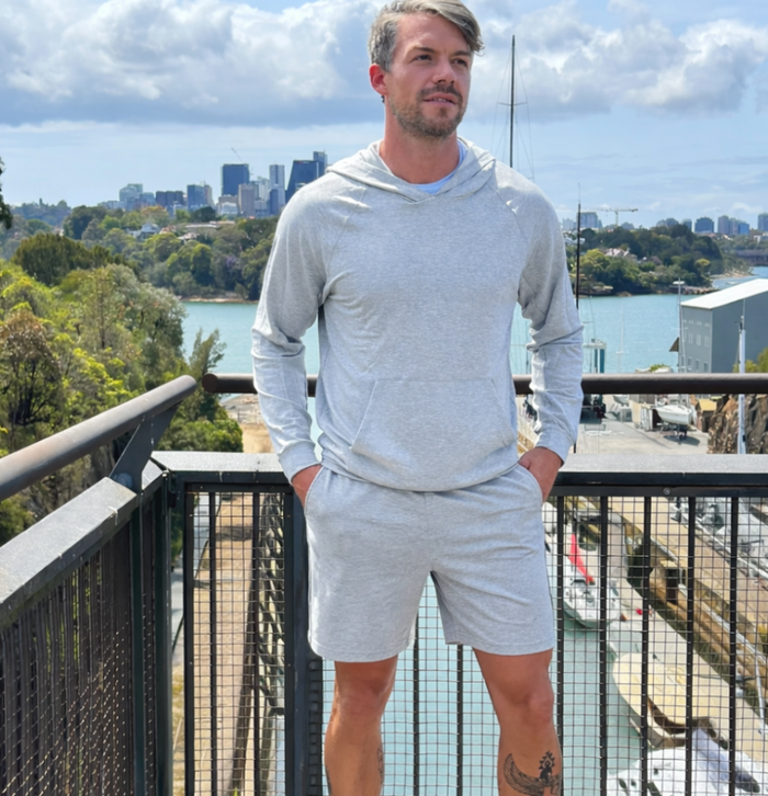 Man in gray hoodie and shorts standing on a balcony with a cityscape in the background